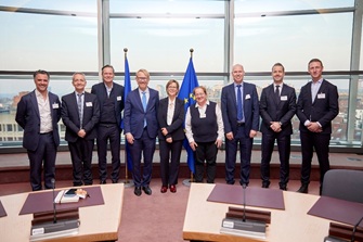 Members of FIA's board and staff standing with Portuguese commissioner Maria Luis Albuquerque, who President von er Leyen has tasked her with overseeing the financial portfolio of the EU, with EU flags in the background.